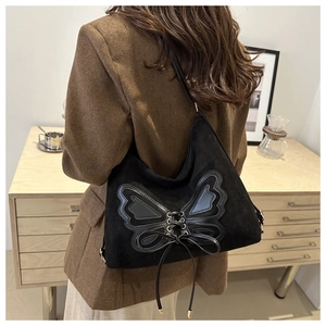 Side view of black suede tote bag with leather butterfly patch and bow detail on a model