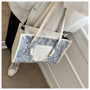 Detail of blue-grey textured shoulder bag with white pearl chain and metal strap