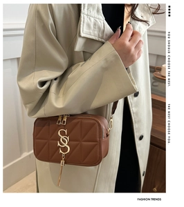 Close-up of brown quilted crossbody bag with gold S-logo and fringe detail on model