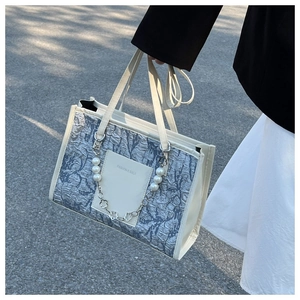Detail of blue and white textured tote bag featuring pearl chain and fashion leather tag
