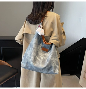 Detail of stone-washed denim tote bag featuring leather straps and plush mascot