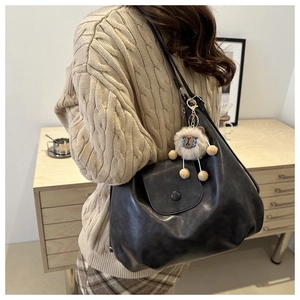 Side view of black matte leather hobo tote bag with plush alpaca charm on wool sweater