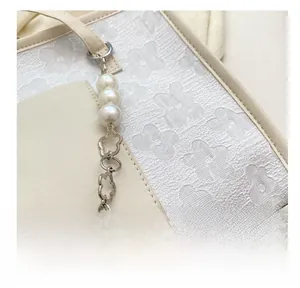 Detailed view of floral jacquard fabric and large pearl metal chain on a cream tote bag