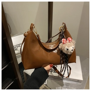 Detail of glossy brown wax leather hobo bag featuring a plush doll charm accessory