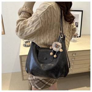 Detail of a black large-capacity tote bag with a cute plush lion charm on soft leather
