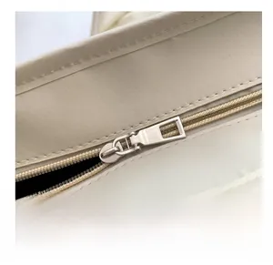 Detail shot of smooth silver metal zipper on cream white leather shoulder bag