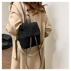 Close-up of a black plush wool backpack with leather straps worn over a khaki trench coat