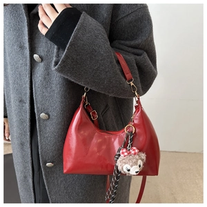 Detail of red gloss faux leather crescent bag with bear charm on a grey wool coat