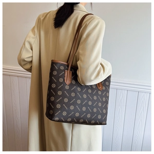 Side view of large printed tote bag in brown pattern worn with a beige trench coat