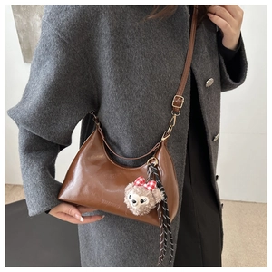 Caramel wax leather crescent bag with adjustable strap and plush pendant on grey coat