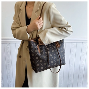 Detail of a large brown monogram tote bag with leather handles on a beige trench coat