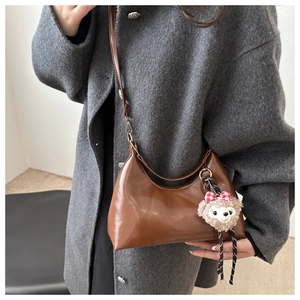 Close-up of brown oil wax leather crescent bag with a plush bear charm on grey coat