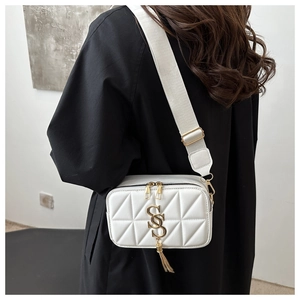 Close-up of white quilted crossbody bag with gold metal logo and tassel detail
