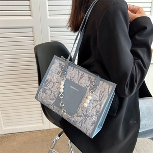 Light blue tote bag with pearl chain and fashion label worn by model in a black suit
