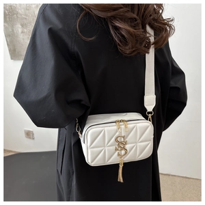 Detail of white quilted crossbody bag with golden dual-S logo and tassel on model