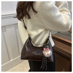 Detail of dark brown glossy crescent bag with shoulder strap and plush charm