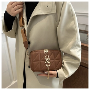 Detail of brown quilted camera bag with gold letter S pendant and tassel strap
