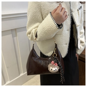 Detail of dark brown leather crescent bag with gold zipper and plush charm on model