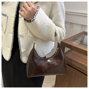 Dark brown patent leather baguette bag with gold hardware worn by model in tweed jacket