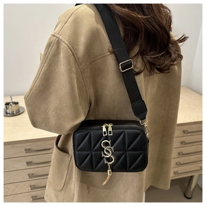 Detail of black quilted crossbody bag featuring golden SS logo and tassel charm