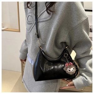 Detail of glossy black leather hobo bag with gold buckle and plush keychain accessory