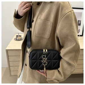 Detail of black quilted crossbody bag with gold metal logo and chain strap on a model