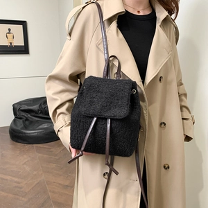 Retro black faux shearling backpack with brown leather straps shown on a beige trench coat