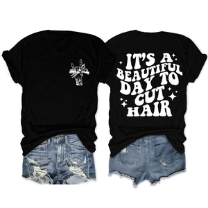 Détail d'un t-shirt noir avec l'inscription 'It's a beautiful day to cut hair' et ciseaux