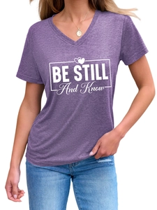 Close-up of purple V-neck T-shirt featuring Be Still And Know graphic text and heart detail