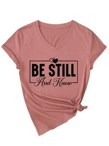 Close-up of pink V-neck t-shirt featuring Be Still And Know text and knot detail