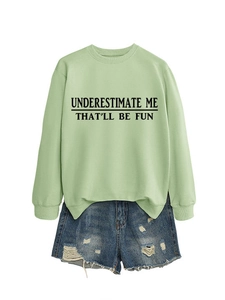 Dettaglio della stampa Underestimate Me That'll Be Fun su felpa verde e pantaloncini denim
