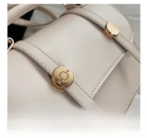 Detail of cream leather shoulder bag showing gold circular buckle and fine stitching