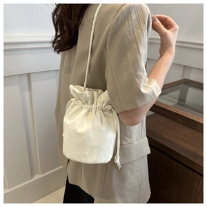 Detail of a beige drawstring bucket bag showing the subtle textured fabric and shoulder strap