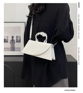 Détail d'un sac géométrique blanc avec poignée en métal argenté fluide sur une chemise noire