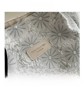 Detail view of large tote bag featuring daisy jacquard fabric and brand logo plate