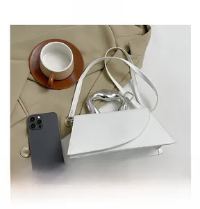 White trapezoidal handbag with unique silver metal handle on a beige suit