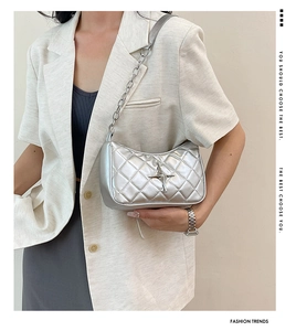 Detail of silver quilted chain bag with star logo worn with a white blazer