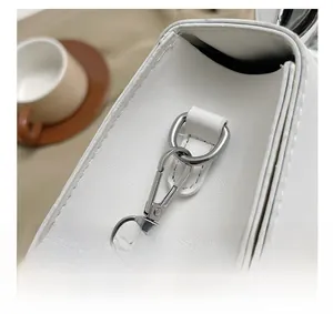 Detail of silver metal hook hardware and lychee grain leather on white crossbody bag