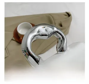Detail of a white square handbag featuring a bold silver chrome curved metal handle