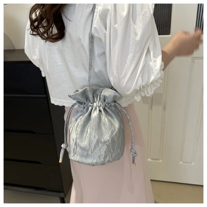 Detail of silver drawstring bucket bag with pleated metallic finish and gold hardware