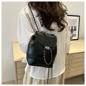 Detail of a black mini leather backpack with a metal chain strap and twist lock on a model
