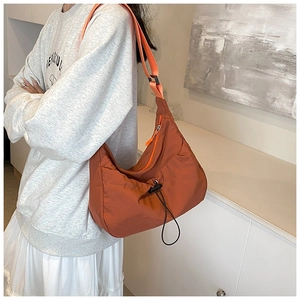 Detail of orange nylon pleated crossbody bag showing drawstring and shoulder strap texture