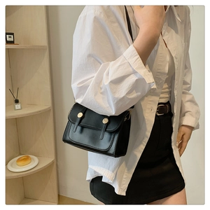 Classic black leather crossbody bag with gold buckle shown on a model in a minimalist setting