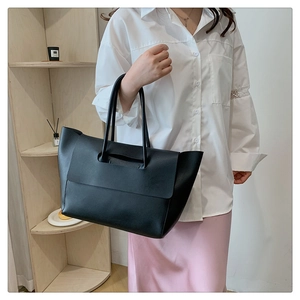 Close-up of large black vintage tote bag with flap and long handles on a model