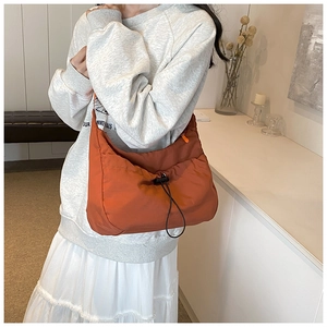 Lifestyle shot of a spacious caramel orange nylon shoulder bag with drawstring detail