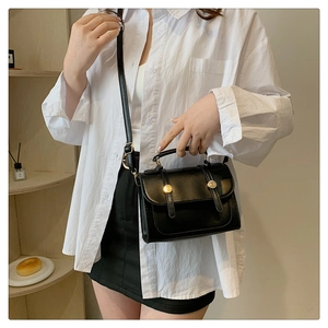 Close-up of retro black leather crossbody bag featuring dual gold cylindrical metal buckles
