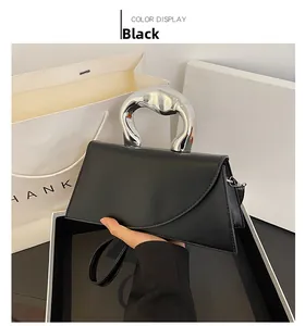 Détail d'un sac à main noir avec une poignée géométrique unique en métal argenté