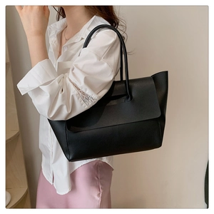 Model wearing a large black leather tote bag with unique flap design and shoulder strap
