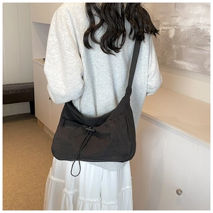 Detail of black pleated crossbody bag with drawstring design worn by a model in interior
