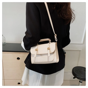 Detail of cream white leather crossbody bag with dual gold metal round buckles and thin strap